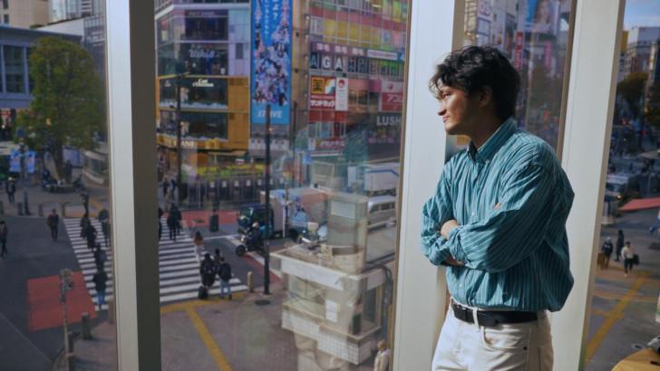 Yasuto accolé à une vitre regardant la rue